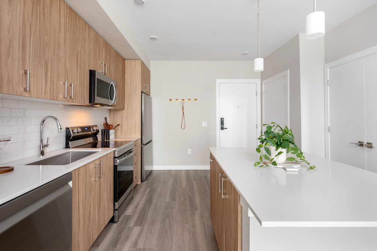 Finish Package II Kitchen with oak cabinetry, white quartz countertops, stainless steel appliances, pendant lighting, and hard-surface vinyl plank flooring - Avalon Westminster Promenade