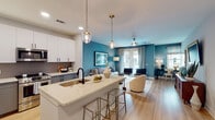 Located at 838 Morrison Dr in Charleston, SC, this single-floor residence at Morrison Yard offers a thoughtfully designed open-concept layout with modern finishes throughout. Light wood flooring flows seamlessly across the entire space, enhancing the bright and airy atmosphere.

The kitchen is a standout feature, boasting two-tone cabinetry with white upper and grey lower cabinets, a quartz waterfall island with bar seating, stainless steel appliances including a side-by-side refrigerator and built-in microwave, a matte black faucet, and a decorative tile backsplash. Pendant lighting with brass accents adds a warm, designer touch above the island.

The open living area is defined by bold teal accent walls, patterned drapery, and French doors that invite natural light and outdoor views. A ceiling fan and recessed lighting ensure comfort throughout the space.

The bedroom features a striking navy accent wall, dual windows with natural light, a ceiling fan, and ample room for a substantial furniture arrangement. An adjacent hallway leads to a well-sized bathroom complete with a dual-sink vanity, grey cabinetry, a marble-tiled glass-enclosed shower, and a convenient stacked in-unit washer and dryer. The overall ambiance is contemporary, polished, and welcoming.