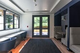 Located at 200 Winchester Cir in Los Gatos, CA, this thoughtfully designed co-working lounge offers a productive and stylish environment within a compact, single-floor footprint. The space is finished with warm hardwood flooring and anchored by a bold navy blue area rug that adds a pop of color and texture to the room.

Natural light pours in generously through large black-framed windows and a set of glass-panel French doors that open to an outdoor patio, offering pleasant views of lush landscaping and the surrounding property. The windows along one wall frame a long, built-in work desk with ample surface area, accompanied by task chairs — an ideal setup for focused, individual work.

Along the opposite wall, a series of semi-private booth-style seating nooks are set into deep navy blue alcoves accented with geometric patterned wallpaper. Each nook features a high-back upholstered chair, a small side table, and a pendant lamp, creating an intimate and comfortable setting for focused work or casual meetings.

The clean white walls and tray ceiling lend the space an open, airy feel, while the cohesive navy and neutral color palette gives it a polished, modern aesthetic. This well-appointed lounge is a functional and inviting workspace suited for both individual productivity and small collaborative sessions.