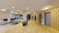 Located at 101 N Grant St in Denver's Capitol Hill neighborhood, this beautifully designed single-floor community space showcases a cohesive mid-century modern aesthetic throughout. Light hardwood flooring flows seamlessly across the expansive open layout, connecting distinct functional zones while maintaining an airy, welcoming atmosphere.

The main lounge area is a standout, appointed with iconic curved shell chairs, plush sofas, and layered area rugs in rich blues and neutrals. Pendant globe light fixtures and recessed lighting illuminate the space, while a built-in fireplace adds warmth and character. Large windows invite natural light and frame views of the surrounding Denver streetscape.

A fully equipped shared kitchen features rich wood cabinetry, white quartz countertops, a stainless steel range with a commercial-style hood, and a white subway tile backsplash — ideal for communal use. Adjacent to the kitchen, a dedicated dining area with a wood conference-style table and mustard upholstered chairs provides a functional gathering space.

Decorative geometric wood screen panels add visual texture near the elevator bank, complementing the warm, curated design language throughout. Package lockers and waste/recycling stations reflect practical, resident-forward amenities. The overall ambiance is polished yet approachable, reflecting thoughtful design at every turn.