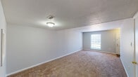 This two-story residence offers two bedrooms and one and a half bathrooms across a well-organized floor plan. The main level features a carpeted living room with neutral gray walls, a textured ceiling, and a front-facing window that allows natural light to fill the space. A pass-through window connects the kitchen to the living area, adding a functional, open feel. The kitchen is equipped with white cabinetry featuring gold hardware, speckled laminate countertops, and an electric range. A half bathroom is also located on the main level, finished with wood-look flooring, white cabinetry, and a tub-shower combination. Upstairs, both bedrooms are carpeted and painted in soft neutral tones with textured ceilings. The primary bedroom includes a ceiling fan with integrated lighting and a window with blinds. The second bedroom also features a window that brings in natural light. The full bathroom on this level includes wood-look flooring, a single-sink vanity with gold hardware, a toilet, and a tub-shower combination. Throughout the home, consistent neutral tones, carpet, and textured ceilings create a cohesive and understated aesthetic.