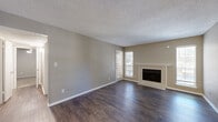 This well-designed 2-bedroom, 1-bathroom single-floor home offers a functional and comfortable layout across a compact yet efficient footprint. The living room serves as the centerpiece of the home, showcasing rich, dark hardwood-style flooring, a textured ceiling, and a classic fireplace framed by a white mantel and flanked by two windows that allow natural light to fill the space. The combined kitchen and dining area features dark cabinetry with light countertops, black appliances including a range and dishwasher, a double sink, and track lighting overhead — providing a practical and stylish cooking environment. A hallway connects the main living areas to the private quarters, where two bedrooms offer plush carpet flooring and ceiling fans. The primary bedroom includes a closet with built-in shelving and a window with outdoor views. The second bedroom also features carpet and a ceiling fan. The shared full bathroom includes dark vanity cabinetry, a double sink, white tile surround, and wood-look flooring. A dedicated closet provides additional storage. Neutral gray and beige tones throughout create a cohesive, move-in-ready aesthetic.