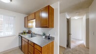 This single-floor unit accommodates five bedrooms and one full bathroom within a efficiently organized floor plan. The layout is connected by four hallways, allowing straightforward navigation between rooms.

The kitchen and living room share an open configuration. The kitchen features warm honey-toned wood cabinetry extending to the upper walls, granite-patterned countertops, a stainless steel range, dishwasher, and a single-basin sink. Tile flooring runs throughout the kitchen, while carpet covers the living area and all bedrooms. The living room opens directly to an outdoor deck through a full-length sliding glass door, providing views of the surrounding exterior.

The five bedrooms are modestly sized, each featuring carpet flooring, neutral walls, and textured ceilings. Most bedrooms include windows with blinds that allow natural light, and baseboard heating units are present in several rooms. The primary bedroom includes a sliding closet.

The single bathroom includes a single-sink vanity with granite-patterned countertop, wood cabinetry, a medicine cabinet with mirror, and a shower-tub combination. Tile flooring completes the space. Throughout the unit, a consistent neutral color palette and textured ceilings create a uniform, understated aesthetic.