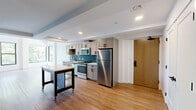 Located at 201 S Huntington Ave in Boston's Jamaica Plain neighborhood, this two-bedroom, one-bathroom unit offers a thoughtfully designed layout across a single floor. The open kitchen and living area serves as the heart of the home, featuring gray shaker-style cabinetry, a striking blue subway tile backsplash, white quartz countertops, and a full suite of stainless steel appliances including a gas range, dishwasher, microwave, and refrigerator. A mobile kitchen island with a butcher block top adds versatile prep and storage space. Warm hardwood-style flooring flows throughout the main living areas, complementing the clean, modern aesthetic. The primary bedroom is a bright, inviting retreat with large corner windows that frame views of surrounding greenery, flooding the room with natural light. The second bedroom features the same light flooring and crisp white walls, offering a clean and flexible space. The bathroom is finished with hexagonal floor tile, white subway tile surrounding the tub-shower combo, and matte black fixtures, with the added convenience of an in-unit stacked washer and dryer. Recessed lighting and a neutral color palette throughout create a cohesive, contemporary ambiance.