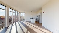 This contemporary single-floor residence showcases a thoughtfully designed open-concept layout that seamlessly connects the living and kitchen areas. The most striking feature is the expansive floor-to-ceiling curtain wall of windows that wraps around the living space, flooding the interior with natural light and offering panoramic views of the surrounding cityscape and neighborhood rooftops. Rich hardwood-style flooring runs throughout the main living areas, complementing the clean, minimalist aesthetic defined by crisp white walls and smooth ceilings.

The kitchen is outfitted with stainless steel appliances, including a refrigerator, range, microwave, and dishwasher, alongside a central island topped with granite countertops and pendant lighting overhead. White cabinetry and light wood flooring complete the kitchen's modern, functional character.

The bedrooms are carpeted for comfort and bathed in natural light through well-placed windows with urban views. One bedroom features a built-in closet with integrated shelving and drawer units, providing generous storage. Each room includes a wall-mounted split-system climate control unit. The bathroom is finished with granite vanity countertops, wood-look vinyl flooring, and a full tub-shower combination, offering a clean and practical space throughout.
