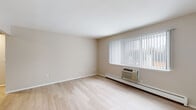This single-floor residence offers a clean, functional layout designed for comfortable everyday living. The open living area is bright and inviting, finished with light wood-tone flooring that extends throughout the main spaces. A large window dressed with vertical blinds fills the room with natural light while offering views of the surrounding outdoors, and a wall-mounted HVAC unit with baseboard heating ensures year-round climate comfort.

The galley-style kitchen is thoughtfully designed with a two-tone cabinetry scheme, pairing crisp white upper cabinets with dark lower cabinets set against a white quartz countertop and a classic subway tile backsplash. Stainless steel appliances — including a refrigerator, electric range, and over-the-range microwave — complete the modern, practical setup. A stainless steel sink with a contemporary faucet adds to the kitchen's polished finish.

The bedroom features plush carpeting, a window with vertical blinds for natural light and privacy, and its own HVAC unit, creating a cozy and quiet retreat. The full bathroom is neatly finished with a tub/shower combo featuring white tile surround, a dark-toned vanity with a white countertop, and wood-tone flooring that ties the space together cohesively.