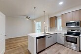 Located at Skyview 331 in Lynnwood, Washington, this single-floor residence showcases a cohesive contemporary design with light wood-tone flooring running consistently throughout the entire space. The open-concept kitchen serves as the central highlight, featuring a peninsula with a white quartz countertop, an undermount sink with a professional-style pull-down faucet, and a full suite of stainless steel appliances including a range, microwave, dishwasher, and refrigerator. Two-toned cabinetry pairs light gray lower cabinets with warm wood-finish upper cabinets, complemented by a classic subway tile backsplash. Pendant lights with globe bulbs hang above the peninsula, while recessed lighting and a ceiling fan illuminate the adjacent living area, which receives natural light through multiple windows with horizontal blinds.

The bedrooms are bright and well-proportioned, with ceiling fans, large windows offering views of surrounding greenery, and sliding-door closets equipped with built-in shelving and hanging rods. The bathrooms maintain the same modern palette, featuring gray vanity cabinets with matte black hardware, white quartz countertops, large mirrors, and light wood-look tile flooring. The overall ambiance is clean, minimalist, and move-in ready.