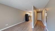 This single-floor unit offers a clean, functional layout with a cohesive design throughout. The open living area flows seamlessly toward the kitchen, creating a spacious and connected feel. Warm-toned, wood-look luxury vinyl flooring extends across the entire unit, adding durability and visual continuity to every room.

The galley-style kitchen is efficiently designed with white cabinetry, dark countertops, and stainless appliances including a gas range and dishwasher. A double-basin sink sits beneath a window that brings in natural light, and ample upper and lower cabinet storage keeps the space practical. A full-size refrigerator anchors the kitchen entrance, visible from the living area.

A dedicated entry hallway with a solid front door provides a welcoming transition into the unit. The bathroom features a white vanity with dark countertop, matching the kitchen's finish palette, and includes a towel bar and wood-look flooring consistent with the rest of the home.

Multiple bedrooms offer comfortable living spaces, each painted in neutral warm-gray tones with white trim and baseboards. The rooms are well-lit by natural light through sizable windows dressed with horizontal blinds or vertical window treatments, offering privacy while maintaining brightness. The overall aesthetic is clean, neutral, and move-in ready.