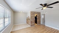 Located in Hanahan, South Carolina, this single-floor, one-bedroom, one-bathroom unit offers a practical and comfortable layout. The living room serves as the welcoming centerpiece of the home, featuring warm wood-look laminate flooring, neutral gray walls, a textured ceiling, and a ceiling fan with light fixture. Natural light filters in through a large window fitted with blinds, while a brick accent column adds a distinctive architectural touch that gives the space character and charm. The transition between the living area and kitchen is marked by a decorative brick arch, adding a rustic element to the overall design. The kitchen area features tile flooring, providing a clean and durable surface. The bedroom offers a comfortable retreat, carpeted for warmth and softness underfoot, with neutral tones on the walls, a ceiling fan, and ample room for furnishings. The bathroom is efficiently appointed with a full tub-shower combination, toilet, and tile flooring. Throughout the unit, clean white trim, consistent neutral wall tones, and textured ceilings create a cohesive and understated aesthetic well-suited for easy, everyday living.