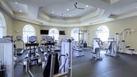 This fitness center is housed within a thoughtfully designed space that balances functionality with architectural elegance. The room features a distinctive octagonal tray ceiling with recessed lighting and dual ceiling fans, lending a sense of elevated volume and airflow throughout the space. Soft yellow walls and large arched windows on multiple sides allow natural light to fill the room, creating a bright and welcoming workout environment.

The facility is well-stocked with a comprehensive range of exercise equipment. Cardio machines, including treadmills, ellipticals, and stationary bikes, are arranged to take advantage of the natural light and views. Multiple strength training machines and cable systems are positioned throughout the space, catering to a variety of workout routines. Wall-mounted flat-screen televisions are installed at strategic viewing angles, enhancing the workout experience.

The dark rubberized flooring provides both durability and safety, offering a stable surface suited for a full range of fitness activities. The combination of ample natural lighting, architectural detail, and a thorough selection of equipment makes this fitness center a functional and attractive amenity.