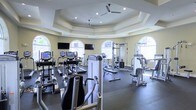 This fitness center is housed within a thoughtfully designed space that balances functionality with architectural elegance. The room features a distinctive octagonal tray ceiling with recessed lighting and dual ceiling fans, lending a sense of elevated volume and airflow throughout the space. Soft yellow walls and large arched windows on multiple sides allow natural light to fill the room, creating a bright and welcoming workout environment.

The facility is well-stocked with a comprehensive range of exercise equipment. Cardio machines, including treadmills, ellipticals, and stationary bikes, are arranged to take advantage of the natural light and views. Multiple strength training machines and cable systems are positioned throughout the space, catering to a variety of workout routines. Wall-mounted flat-screen televisions are installed at strategic viewing angles, enhancing the workout experience.

The dark rubberized flooring provides both durability and safety, offering a stable surface suited for a full range of fitness activities. The combination of ample natural lighting, architectural detail, and a thorough selection of equipment makes this fitness center a functional and attractive amenity.