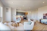 Located at 17 Avenue E in Bayonne, NJ, this well-designed 2-bedroom, 1-bathroom residence offers a bright and contemporary living experience across a single floor. The open-plan living, dining, and kitchen area is anchored by light hardwood flooring and crisp white walls, creating an airy, cohesive feel. Recessed lighting complements the abundant natural light streaming through large windows. The kitchen is outfitted with two-tone cabinetry — matte dark upper cabinets paired with warm wood lower cabinets — white quartz countertops, under-cabinet lighting, and a full suite of stainless steel appliances including a gas range, dishwasher, microwave, and refrigerator. The primary bedroom is a comfortable retreat featuring a built-in closet and oversized windows that frame open views of the Bayonne skyline and green treetops. The second bedroom also benefits from a large window with similarly pleasant outdoor views. The bathroom showcases a striking marble-effect accent wall, a round backlit mirror, a dark vanity with white countertop, large-format tile flooring, and a tub-shower combination. Additional spaces include a laundry area, closet, and utility room, enhancing overall functionality. The home presents a clean, modern aesthetic throughout.