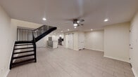This two-floor space offers a thoughtfully designed layout with a clean, modern aesthetic throughout. The lower level features a spacious open living area with large light-toned tile flooring, recessed lighting, and a ceiling fan. A striking black metal staircase serves as a functional design element, connecting both floors. The fully equipped kitchen is a standout feature, showcasing white shaker-style cabinetry, granite countertops, a dark mosaic tile backsplash, and a full suite of stainless steel appliances including a refrigerator, range, microwave, and dishwasher. A sliding barn door adds a contemporary touch near the main living area. A half bathroom on the lower level includes a granite-topped vanity and tile flooring. The upper level transitions to rich, dark hardwood-style flooring and features multiple well-sized bedrooms, each equipped with ceiling fans. One bedroom includes French doors and access to a walk-in closet, while another benefits from a bright window with blinds. A full bathroom upstairs is elegantly tiled with white subway tile and accented by a decorative blue penny-tile border in the tub-shower combination. The overall ambiance is bright, clean, and move-in ready.