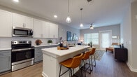 Located at 3125 Fire Ct in Charlotte, NC, this single-floor residence offers a thoughtfully designed open-concept layout that seamlessly connects the kitchen, dining, and living areas. The kitchen is a standout feature, showcasing two-tone cabinetry with white upper cabinets and gray lower cabinets, a white quartz countertop island with an undermount sink, pendant lighting, a subway tile backsplash, and a full suite of stainless steel appliances. A built-in desk nook adjacent to the kitchen provides a dedicated workspace. The living room is bright and inviting, benefiting from generous natural light through large windows, a ceiling fan, and direct access to an outdoor area. The bedroom is well-sized, offering dual windows with outdoor views and warm wood-look flooring that continues throughout the unit. The bathroom is finished with gray shaker-style cabinetry, a white quartz vanity top, a large mirror, and a full tub-shower combination. Consistent wood-look flooring, neutral gray walls, and recessed lighting unify the space with a clean, modern aesthetic throughout.