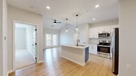 This single-story, 3-bedroom, 1-bathroom home offers a thoughtfully designed open-concept layout that maximizes its generous floor area. The heart of the home is the kitchen and dining space, where a central island with a granite countertop and an undermount sink with a matte black faucet serves as a stylish focal point. White shaker-style cabinetry with black hardware lines the walls, complemented by a subway tile backsplash and a full suite of stainless steel appliances, including a refrigerator with ice dispenser, electric range, and built-in microwave. Globe pendant lights hang above the island, adding a modern touch. Light hardwood flooring flows throughout the main living areas, while vaulted ceilings in the living space and a ceiling fan enhance the airy, open feel. A glass-paned door provides access to the outdoors, filling the space with natural light. Each of the three bedrooms features plush carpeting, ceiling fans, and windows with slatted blinds that invite natural light. The primary bedroom offers a generous footprint with ample room for furnishings. The bathroom is finished with a granite-topped gray vanity, wood-look flooring, and matte black hardware accents, maintaining a cohesive modern aesthetic throughout.