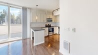 Located at 14307 Greenwood Ave N in Seattle, WA, this well-appointed one-bedroom, one-bathroom unit offers a thoughtfully designed layout across a single floor. Warm hardwood-style flooring flows throughout the space, complemented by crisp white walls and clean modern finishes.

The open-concept kitchen, dining, and living area serves as the heart of the home. The kitchen is outfitted with stainless steel appliances including a range, microwave, and dishwasher, paired with white shaker-style cabinetry, gray countertops, a white subway tile backsplash, and track lighting overhead. A peninsula provides additional prep and seating space. Floor-to-ceiling windows and a private balcony off the living area bring in abundant natural light.

The bedroom is a comfortable, well-proportioned room with its own dedicated closet featuring wire shelving for organized storage. The full bathroom includes a soaking tub with shower, large-format white tile flooring, and a clean, minimalist design.

A dedicated laundry room with a full-size washer and dryer adds everyday convenience. A hallway connects all areas seamlessly. The overall ambiance is modern, bright, and functional — ideal for those seeking a clean, move-in-ready home in Seattle's vibrant Greenwood neighborhood.