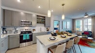 Located at 7200 N Frontage Rd in Orlando, Florida, this single-floor residence offers a thoughtfully designed layout with contemporary finishes and a cohesive modern aesthetic. The kitchen is a standout feature, showcasing gray shaker-style cabinetry extending to the ceiling, stainless steel appliances including a French door refrigerator, electric range, and over-the-range microwave, paired with granite countertops and a herringbone tile backsplash. A large kitchen island with seating provides both additional workspace and a casual dining option, illuminated by stylish pendant lighting and wood-look flooring. The open living area is bright and inviting, featuring large windows that allow ample natural light, a ceiling fan, and hardwood-style flooring that flows seamlessly throughout. The bedrooms offer plush carpeting, generous closet space, and large windows. The primary bedroom connects to a well-sized bathroom featuring marble-look tile flooring, a granite-topped vanity with gray cabinetry, and a tub-shower combination. An additional bathroom mirrors the same quality finishes. Throughout the residence, a neutral color palette is accented by modern fixtures, creating a clean and functional living environment.