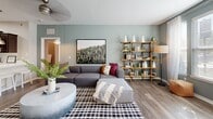 This thoughtfully designed single-floor residence offers a cohesive blend of modern finishes and functional living spaces. The kitchen is a standout feature, showcasing rich dark wood cabinetry, stainless steel appliances including a French door refrigerator, a gas range, and a built-in microwave, all complemented by a white quartz countertop and classic subway tile backsplash. Wood-look flooring runs throughout the main areas, while a large breakfast bar with pendant lighting provides a seamless connection to the living space. The living room is anchored by sage-green accent walls, wood-look flooring, and generous natural light, creating an inviting and relaxed atmosphere. The primary bedroom features a bold dark accent wall, plush carpeting, and multiple windows, with direct access to a private en-suite bathroom equipped with a single vanity, dark cabinetry, tile flooring, and a walk-in closet with built-in shelving. A second bedroom offers carpet flooring and ample natural light with outdoor views. A dedicated home office or flex room features hardwood-style floors and large windows. The in-unit laundry room accommodates a full-size washer and dryer with overhead wire shelving for added storage.