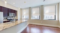 This thoughtfully designed one-bedroom, one-bathroom residence offers a functional and stylish layout across a single floor. The open-concept kitchen and living area serves as the heart of the home, featuring rich hardwood flooring, large windows with roller shades that invite generous natural light, and a ceiling fan for added comfort. The kitchen is equipped with dark espresso cabinetry, stainless steel appliances including a refrigerator, microwave, and range, a tile backsplash, and a granite-topped peninsula that provides both prep space and a casual dining option, illuminated by sleek pendant lighting. The bedroom is a comfortable, well-proportioned space with hardwood floors, a ceiling fan, and a clerestory window that allows in natural light while maintaining privacy. It is complemented by a dedicated closet featuring built-in shelving and hanging rods for organized storage. The bathroom is elegantly finished with marble-look tile on both the floors and shower surround, a soaking tub with glass partition and handheld showerhead, and chrome fixtures throughout. A convenient in-unit stacked washer and dryer is tucked into the hallway, adding everyday practicality. Neutral warm-toned walls and white trim create a clean, cohesive aesthetic throughout the entire residence.