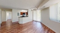 This single-floor residence offers a practical and comfortable layout across two bedrooms and two bathrooms. The open-concept kitchen and living area serves as the heart of the home, featuring rich wood-look flooring, warm-toned cabinetry, dark countertops, and a peninsula with an integrated sink — ideal for both cooking and casual dining. Black appliances and track lighting add a modern touch, while a large bank of windows dressed with vertical blinds fills the living area with abundant natural light and provides views of lush greenery outside.

The hallways connect the living spaces to the private quarters and are fitted with wood-look flooring and flush ceiling lighting. Both bedrooms feature plush carpet flooring and windows that invite natural light. The generously sized primary bedroom includes direct access to one of the two bathrooms, offering added privacy. The second bedroom features a built-in closet with bifold louvered doors, providing practical storage. Both bathrooms are finished consistently, with warm wood-toned vanities, white countertops, tub-shower combinations with white surrounds, and durable wood-look tile flooring. The overall aesthetic throughout the space is clean, neutral, and move-in ready.