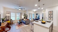 This single-story residence is designed with a contemporary open-concept layout that seamlessly connects the kitchen, dining, and living areas. The kitchen is a functional centerpiece, featuring dark espresso cabinetry, stainless steel appliances including a refrigerator, range, and microwave, and an expansive granite-topped island with seating for multiple occupants. Pendant lighting above the island adds a polished accent, while recessed lighting throughout ensures consistent illumination.

The living area is generously proportioned, accommodating comfortable seating arrangements beneath a ceiling fan. Multiple windows allow natural light to flow freely, offering outdoor views and contributing to the bright, airy atmosphere. Light wood-style flooring runs throughout the main living spaces and bedroom, creating visual continuity.

The bedroom is a well-sized retreat with a large window framing outdoor views, flanked by ample wall space. A walk-in closet with shelving provides practical storage. The bathroom is cleanly finished with a granite-topped vanity featuring dark cabinetry, a tub-shower combination with tiled surround, and wood-style flooring consistent with the rest of the unit. Overall, the space presents a cohesive, modern aesthetic with neutral tones and quality finishes throughout.