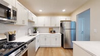 This single-floor, 2-bedroom, 2-bathroom residence offers a thoughtfully designed layout that maximizes every square foot. Light wood-tone flooring runs throughout, creating a warm, cohesive aesthetic across all rooms.

The kitchen is a standout feature, showcasing white shaker cabinetry with brushed nickel hardware, light stone countertops, a classic subway tile backsplash, and stainless steel appliances including a refrigerator, dishwasher, and range. Recessed lighting illuminates the space efficiently.

Adjacent to the kitchen, the dining area provides an intimate setting with neutral warm-toned walls, and the living room offers generous space accented by a textured ceiling and a sliding glass door that invites natural light and outdoor views. The open flow between these areas enhances the sense of space.

The primary bedroom is comfortably sized with a window providing natural light and views of the outdoors. The second bedroom also features a window and ample floor space. Both bathrooms are finished with white vanities, brushed nickel fixtures, and wood-look flooring, maintaining the home's clean, modern aesthetic.

Two hallways connect the rooms efficiently, and the neutral warm-beige wall palette throughout lends the entire residence a bright, inviting, and move-in-ready appeal.