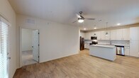 This single-story residence offers a thoughtfully designed open-concept layout that connects the living and kitchen areas seamlessly. The living room is bright and welcoming, benefiting from multiple windows and a set of French doors that invite natural light while providing direct outdoor access. A ceiling fan overhead adds both comfort and style to the space, which is finished with warm-toned wood-look flooring throughout.

The kitchen is a standout feature, showcasing white shaker-style cabinetry, granite-look countertops, and a classic subway tile backsplash. Stainless steel appliances — including a refrigerator, electric range, built-in microwave, and dishwasher — complement the space, while pendant lighting above the kitchen island adds a modern touch.

The bathroom is well-appointed with an extended granite-topped vanity, a large mirror, and continued wood-look flooring for a cohesive aesthetic. The bedroom includes access to a spacious walk-in closet with built-in wire shelving and carpeted flooring.

A dedicated laundry area houses a full-sized washer and dryer, adding everyday convenience. The unit's neutral palette and consistent finishes throughout create a clean, modern ambiance.