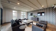 Located at 4015 Aspen Grove Drive in Franklin, Tennessee, this stylish single-floor lounge space is designed with a refined, contemporary aesthetic that blends comfort and sophistication. The main gathering area is anchored by warm hardwood flooring laid in a herringbone-influenced pattern, complemented by a striking geometric wallcovering that serves as a bold focal point. Mounted flat-screen televisions and a substantial herringbone-front media credenza enhance the entertainment-focused layout. The ceiling features a distinctive linear paneled design with recessed lighting that adds architectural depth and a warm, inviting ambiance. Generously sized windows along one wall flood the interior with natural light and frame views of the surrounding Franklin cityscape. Tufted leather seating, a large rustic wood coffee table, and layered area rugs contribute to the space's upscale yet approachable character. A well-appointed wet bar area with subway tile backsplash, gray cabinetry, under-counter refrigeration, and a stainless steel sink provides excellent functionality for entertaining. On the opposite side of the room, a set of French doors opens directly onto a spacious outdoor terrace, where additional seating areas and sweeping views of the Tennessee hills create an exceptional extension of the interior living space.