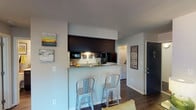 Located at 4500 E 82nd St in Indianapolis, IN, this single-floor residential unit offers a well-designed layout with a cohesive modern aesthetic throughout. The kitchen is a standout feature, boasting granite countertops, dark espresso cabinetry, hardwood-style flooring, and black appliances. A galley-style configuration maximizes counter space on both sides, while a dedicated pantry provides generous storage. The kitchen opens to a breakfast bar with seating, creating a natural transition into the living area. The living room is bright and welcoming, with a large window that draws in natural light and provides a comfortable, open atmosphere. The bedroom offers plush carpeting, ample dresser space, and a sliding glass door that opens to an outdoor area, filling the room with additional natural light and outdoor connectivity. A second bedroom features soft carpeting and warm ambient lighting. The bathroom is clean and functional, with a dark vanity cabinet, white countertop, a well-lit mirror, and modern brushed nickel fixtures. A laundry area is conveniently accessible within the unit. Throughout the space, hardwood-style flooring in the main areas and soft carpet in the bedrooms provide both durability and comfort, contributing to a cohesive and inviting living environment.