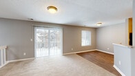 Located at 3855 Oak Lake Cir in Indianapolis, Indiana, this two-story home offers a practical and well-organized layout spread across two levels. The entry level provides access to a carpeted staircase with white railings and a window that draws in natural light, leading up to the main living floor above.

The upper level hosts the majority of the living space, beginning with an open-concept kitchen and living room combination. The kitchen is outfitted with warm wood cabinetry, light countertops, stainless steel appliances, and light hardwood-style flooring, along with a convenient breakfast bar. The adjacent living area features a mix of carpet and hardwood-style flooring, neutral taupe walls, a textured ceiling, and large sliding glass doors that flood the room with natural light and provide outdoor views.

The spacious bedroom is carpeted and painted in soft gray tones, featuring dual side-by-side closets that offer generous storage. Corner windows allow ample natural light into the room. The full bathroom includes a wood-toned vanity with a stone-look countertop, a tiled shower-tub combination, and durable wood-look plank flooring. Throughout the home, neutral gray and taupe color palettes create a cohesive and calm atmosphere.