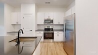 Located at 720 River Hwy in Mooresville, NC, this well-appointed one-bedroom, one-bathroom residence offers a thoughtfully designed single-floor layout with a clean, modern aesthetic throughout. The open-concept kitchen and living area serves as the heart of the home, featuring crisp white shaker cabinetry with matte black hardware, dark granite countertops, a center island with an undermount sink and sleek black faucet, and a full suite of stainless steel appliances including a refrigerator with ice maker, electric range, and built-in microwave. A subtle tile backsplash and recessed lighting complete the kitchen's contemporary look, while light hardwood-style flooring extends seamlessly into the living area. The spacious bedroom offers generous square footage, plush carpeting, a ceiling fan, and multiple windows that invite ample natural light. The bathroom is finished with a sliding-glass enclosed shower, matte black fixtures, and matching dark granite counters for a cohesive feel. A dedicated laundry room with full-size washer and dryer and overhead shelving adds everyday convenience. The space is finished in a neutral, bright palette throughout, creating a fresh and inviting atmosphere well-suited for comfortable living.