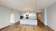 Located at 3101 Euclid Ave in Cleveland's vibrant Midtown corridor, this well-appointed 2-bedroom, 3-bathroom residence offers a thoughtfully designed single-floor layout. The open-concept kitchen and living area serves as the heart of the home, anchored by a large central island with granite countertops and an undermount sink. White shaker cabinetry, black appliances, and track lighting complete the kitchen's clean, modern aesthetic. Hardwood-style flooring runs throughout the main living areas, enhancing the bright, airy feel of the space. The primary bedroom is a comfortable retreat featuring large windows with urban views of the Cleveland skyline and surrounding neighborhood, along with track lighting and generous closet space, including a walk-in closet with dual hanging rods and shelving. The second bedroom also offers hardwood-style floors and track lighting. The bathrooms are finished with tile flooring; the primary bath includes a glass-enclosed shower and a vanity topped with granite countertops and dark wood cabinetry. Two hallways connect the rooms efficiently, and a dedicated utility room adds practical functionality. With four closets total and a clean, neutral color palette throughout, this residence combines modern finishes with a versatile, livable floor plan.