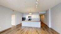Located at 3101 Euclid Ave in Cleveland's vibrant Midtown corridor, this well-appointed 2-bedroom, 3-bathroom residence offers a thoughtfully designed single-floor layout. The open-concept kitchen and living area serves as the heart of the home, anchored by a large central island with granite countertops and an undermount sink. White shaker cabinetry, black appliances, and track lighting complete the kitchen's clean, modern aesthetic. Hardwood-style flooring runs throughout the main living areas, enhancing the bright, airy feel of the space. The primary bedroom is a comfortable retreat featuring large windows with urban views of the Cleveland skyline and surrounding neighborhood, along with track lighting and generous closet space, including a walk-in closet with dual hanging rods and shelving. The second bedroom also offers hardwood-style floors and track lighting. The bathrooms are finished with tile flooring; the primary bath includes a glass-enclosed shower and a vanity topped with granite countertops and dark wood cabinetry. Two hallways connect the rooms efficiently, and a dedicated utility room adds practical functionality. With four closets total and a clean, neutral color palette throughout, this residence combines modern finishes with a versatile, livable floor plan.