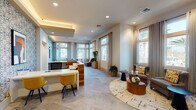 This thoughtfully designed single-floor community space blends contemporary aesthetics with functional layouts to create a welcoming and professional environment. At its heart is a sleek reception area, anchored by a warm wood-paneled front desk set against a bold patterned accent wall, complemented by cove lighting, large-format tile flooring in a herringbone pattern, and floor-to-ceiling windows that flood the space with natural light. Vibrant yellow accent chairs add a pop of color alongside curated artwork.

The adjacent lounge area features a striking birch-tree-patterned wallcovering, a wall-mounted TV, plush sectional seating, and an eclectic live-edge coffee table, with decorative lattice partitions separating it from a cozy nook workspace. A separate casual gathering area offers a long white conference table with seating for a large group and wood-look tile flooring, while a dedicated conference room accommodates formal meetings around a hardwood table beneath a triptych of framed art.

The expansive clubroom boasts light hardwood flooring, a granite-topped island with bar seating, globe pendant lighting, a wall-mounted TV, and direct glass door access to an outdoor pool courtyard. Additional amenities include accessible restrooms, a quiet reading nook with tall windows and plush seating, and neatly appointed hallways throughout.