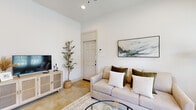 Located at 33455 Buckshot Ln in Magnolia, Texas, this single-story home offers a clean, modern aesthetic rooted in neutral tones and natural materials throughout. The living room greets you with soaring ceilings, polished concrete floors, and abundant natural light, creating an airy and welcoming atmosphere. A comfortable seating area anchors the space, complemented by tasteful wall art and a cane-front media console.

The open-concept kitchen is a standout feature, boasting white shaker cabinetry, a center island with bar seating, stainless steel appliances, and warm pendant lighting. It flows seamlessly into a dining area illuminated by a stylish chandelier and accented by a rustic wood dining table — ideal for everyday meals or entertaining.

Two well-appointed bedrooms feature plush carpeting, large windows that invite natural light and outdoor views, and ample space for furnishings. The full bathroom offers a dual-sink vanity with white quartz countertops, white cabinetry, and a tiled shower, combining practicality with a clean, crisp design.

A dedicated laundry room with overhead cabinetry and full-size washer and dryer connections adds everyday convenience. Throughout the home, polished concrete floors, recessed lighting, and a cohesive soft palette create a calm, functional living environment.