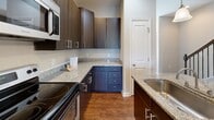 Located at 10154 Enniscrone Rd in Pineville, NC, this three-bedroom, five-bathroom home spans three thoughtfully laid-out floors. The entry level provides a compact yet functional foundation, while the main floor serves as the heart of the home, offering a combined kitchen and living area. The kitchen is well-appointed with dark espresso cabinetry, granite countertops, stainless steel appliances including a refrigerator, range, and built-in microwave, and warm hardwood flooring. A pendant light accent and a kitchen island add both style and practicality. The living area continues the hardwood flooring and features a pendant light fixture, creating a cohesive and inviting atmosphere. The upper floor houses the bedrooms, including a generously sized primary bedroom with plush carpeting and natural light from multiple windows overlooking the surrounding neighborhood. The additional bedrooms also feature soft carpet flooring. All five bathrooms are finished with granite-topped vanities, white cabinetry, and large mirrors. A carpeted staircase with a rich wood handrail and black iron balusters connects the floors with classic elegance. Throughout the home, neutral wall tones and clean white trim provide a timeless, move-in-ready aesthetic.