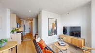 Located in Chicago's vibrant Lincoln Park/Clybourn Corridor area, this thoughtfully designed one-bedroom, one-bathroom residence makes excellent use of its compact footprint. The open-plan living area is bright and airy, anchored by crisp white walls, warm light wood flooring, and a large floor-to-ceiling window that frames sweeping views of the Chicago skyline and surrounding cityscape, flooding the space with natural light.

The kitchen runs along one wall in a galley configuration, featuring flat-front light wood cabinetry extending to the ceiling for ample storage, stainless steel appliances including a gas range, built-in microwave, dishwasher, and refrigerator, complemented by a white herringbone tile backsplash and clean quartz countertops.

The bedroom is a cozy, efficiently laid-out retreat, separated from the main living and kitchen corridor by a dividing wall. The bathroom offers a clean, minimalist aesthetic with light wood vanity cabinetry, a white countertop, tiled flooring, and a walk-in shower with tub. In-unit laundry and a closet round out the practical amenities. Throughout, the design maintains a consistent modern palette of warm wood tones and white finishes, creating a cohesive and inviting atmosphere.