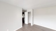 This single-floor unit offers a practical and well-maintained layout across several clearly defined living spaces. The living room is the largest area of the unit, featuring light-toned laminate flooring, neutral grey walls, and a wide window fitted with vertical blinds that allows natural light to fill the room. A baseboard heater runs along the exterior wall, providing efficient in-room heating. The living area connects to a bedroom that mirrors its clean aesthetic, also finished with laminate flooring and neutral tones, complete with a built-in closet for storage. A second bedroom is similarly appointed with laminate flooring, a window with outdoor views of the surrounding neighbourhood, a baseboard heater, and clean white walls. Both bedrooms offer dedicated closet space. The kitchen is compact and functional, equipped with dark espresso cabinetry, laminate countertops, a stainless steel single-basin sink, and a black electric range. The bathroom includes a full-size soaker tub with an overhead shower and white surround panels, a toilet, and a vanity with storage, all finished with dark laminate flooring. Throughout the unit, consistent use of light neutral paint, white trim, and laminate flooring creates a cohesive and move-in-ready atmosphere.