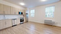 Located at 11 1st Ave in Bay Shore, NY, this efficiently designed single-floor unit offers a bright and modern living environment. The open-concept layout seamlessly connects the kitchen and living room, creating a functional and inviting space. Light hardwood-style flooring runs throughout, lending warmth and visual continuity to every room.

The kitchen is well-appointed with light wood cabinetry, a white subway tile backsplash, clean countertops, and a full suite of stainless steel appliances including a refrigerator, range, dishwasher, and over-the-range microwave. Multiple windows fitted with horizontal blinds allow abundant natural light to fill the living area, which also features a wall-mounted climate control unit.

The bathroom is finished to a high standard, showcasing a full tub and shower combination with white subway tile surround, chrome fixtures, a floating wood vanity with a white countertop, and a large mirror. The space also includes a dedicated utility area with an in-unit stacked washer and dryer alongside a water heater, as well as a closet with a hanging rod for additional storage. The overall aesthetic is clean, contemporary, and move-in ready.