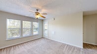 This single-story unit offers a functional and efficiently organized layout across a compact footprint. The kitchen is a standout feature, designed in a galley style with white cabinetry, granite-style countertops, light hardwood-style flooring, stainless steel appliances including a refrigerator and range, and a peninsula with a sink that opens toward the living area — creating a convenient pass-through feel. The living room is carpeted and bright, featuring a ceiling fan with light fixture, a textured ceiling, and large windows that allow generous natural light and views of surrounding greenery. A door from the living area provides direct access to a private balcony. A second carpeted area serves as an additional living or dining space, also equipped with a ceiling fan and balcony access via sliding doors with vertical blinds. The bedroom is a comfortable size, finished with carpet, a textured ceiling, and a closet with bifold doors. The bathroom features a full tub-shower combination with white tile surround, wood-style flooring, a vanity with mirror, and clean, neutral finishes throughout. Overall, the unit presents a neutral, light palette with consistent finishes.