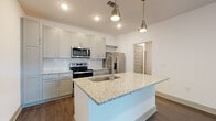 Located at 2789 Satellite Blvd in Duluth, GA, this well-appointed one-bedroom, one-bathroom residence offers a thoughtfully designed single-level layout. The interior is defined by dark hardwood-style flooring that flows seamlessly through the main living areas, complemented by crisp white walls and recessed lighting that keep the space bright and clean.

The kitchen serves as the centerpiece of the home, showcasing a large central island with a granite countertop and integrated sink, illuminated by sleek industrial-style pendant lights. Gray shaker cabinetry lines the walls alongside a classic white subway tile backsplash, and the space is fully equipped with a full suite of stainless steel appliances, including a refrigerator with ice maker, electric range, microwave, and dishwasher.

A hallway with a modern paneled door connects the main living area to the private quarters. The bedroom is a comfortable, carpeted retreat featuring a ceiling fan and a wide window dressed with horizontal blinds, allowing for natural light and outdoor views. The bathroom is finished with a granite-topped vanity with gray cabinetry, a tiled tub-shower combination, and coordinating hardwood-style flooring. The overall design aesthetic is modern and neutral, offering a clean, move-in-ready environment.