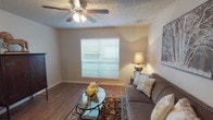 This single-story 1-bedroom, 1-bathroom residence offers a thoughtfully designed layout that maximizes comfort and functionality. The living room serves as the heart of the home, featuring warm wood-look flooring, a ceiling fan with integrated lighting, and a large window fitted with blinds that invites natural light while maintaining privacy. The space flows naturally into a dedicated dining area, which continues the wood-look flooring and is accented by a decorative sunburst mirror, creating an inviting atmosphere for everyday dining. The galley-style kitchen offers ample cabinetry with dark finishes, granite-look countertops, a double-basin sink, and full-size appliances including a refrigerator and dishwasher, with additional storage accessible at the rear. The bedroom is a comfortable retreat, carpeted for warmth, with a large window that brings in natural light and enough space to accommodate a full furniture arrangement. The full bathroom features a combined tub and shower with tile surround, a vanity with granite-look countertops, dark cabinetry, and wood-look flooring. Textured ceilings are found throughout, and the neutral color palette provides a cohesive, move-in-ready aesthetic across all rooms.