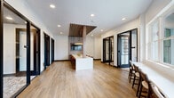 Located at 4455 Condor Dr in Hilliard, Ohio, this thoughtfully designed professional workspace offers a polished, contemporary environment ideal for productivity and collaboration. The single-floor layout is anchored by light-toned hardwood flooring that flows throughout, creating a cohesive and inviting atmosphere.

The space features multiple glass-enclosed rooms framed in sleek black metal, providing both visual transparency and acoustic privacy. A dedicated conference room is outfitted with a large table, ergonomic rolling chairs, and a distinctive sculptured pendant light, all set against a textured stone accent wall — making it well-suited for formal meetings. Additional glass-walled private offices and focus rooms line the perimeter, each accessible through black-framed glass doors that reinforce the modern aesthetic.

An open collaborative area offers counter-height seating along windowed walls, allowing natural light to fill the space and providing views of the surrounding exterior. A standout feature is a private meeting nook designed with rich wood slatted wall paneling, a wall-mounted display, and leather barrel chairs arranged around a white communal table — lending warmth and sophistication to the interior.

The overall ambiance balances professionalism with comfort, combining crisp white walls, recessed lighting, and refined design details throughout.