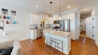 This two-story home is thoughtfully designed with a consistent aesthetic of clean white walls, rich hardwood flooring, and black hardware accents throughout. The entry foyer welcomes visitors with a stately staircase featuring warm wood treads, white risers, and a classic turned newel post, setting an inviting tone for the rest of the home.

The main living area centers around a standout marble-surround fireplace, complemented by hardwood floors and generous natural light streaming through large windows dressed with layered curtains. The kitchen is a functional and stylish centerpiece, showcasing white shaker cabinetry, granite countertops, stainless steel appliances, and a granite-topped island with seating for multiple guests, illuminated by pendant lighting overhead.

The bathrooms are finished with marble-tile surrounds, granite vanity tops, white shaker cabinetry, and matte black fixtures, offering a refined yet timeless look. Bedrooms are carpeted for comfort, with natural light provided by windows fitted with blinds. One upper-level room features a tray ceiling, adding architectural interest. An additional bedroom offers a cozy, minimalist retreat. Throughout the home, crown molding, recessed lighting, and consistent design choices contribute to a cohesive and polished living environment across both floors.