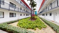 This 310 square foot apartment, located at 6925 W 16th Ave in Hialeah, Florida, offers a modern and efficient living space. The single-floor layout comprises a kitchen, bathroom, and utility room, maximizing functionality within its compact footprint. The exterior showcases a tropical-inspired design with white-painted buildings accented by vibrant red trim. Lush landscaping, including palm trees and colorful foliage, creates an inviting courtyard area between the apartment blocks. The kitchen features contemporary white cabinetry, stainless steel appliances, and light-colored countertops, providing a bright and clean aesthetic. The bathroom continues this theme with a white vanity, large mirror, and modern fixtures. Light-colored flooring throughout enhances the sense of space, while large windows allow for ample natural light. The property's exterior offers a balcony or walkway, providing outdoor access and views. This apartment combines efficiency with style, ideal for those seeking a cozy yet well-appointed living space in a vibrant Florida setting.