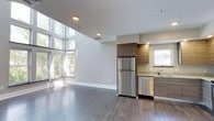 This two-story residence offers a thoughtfully designed layout across three bedrooms and two bathrooms. The open-concept main level immediately impresses with soaring double-height windows that flood the living area with generous natural light, creating a bright and airy atmosphere. Rich, dark hardwood flooring extends throughout, adding warmth and visual continuity to the space.

The kitchen is seamlessly integrated into the main living area and is outfitted with stainless steel appliances, including a full-size refrigerator and dishwasher. Warm wood-toned cabinetry provides ample storage, while granite countertops lend a polished, contemporary finish. A window above the sink brings in additional natural light, enhancing the kitchen's functional appeal.

The open living area benefits from the dramatic vertical scale created by the two-story window wall, making the space feel expansive and connected to the outdoors. Neutral wall tones and clean architectural lines contribute to a modern, understated aesthetic throughout. The overall ambiance is one of refined comfort, balancing contemporary design with practical livability across both floors.