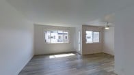 This well-appointed 1-bedroom, 1-bathroom residence is thoughtfully laid out on a single floor, offering a comfortable and functional living environment. The open living area is bathed in natural light, courtesy of multiple large windows that frame views of the surrounding neighborhood and allow sunlight to pour across the smooth hardwood-style flooring. Clean white walls and bright ceilings lend the space an airy, modern feel throughout. A glass-panel door provides additional light and convenient access to the exterior. The layout flows efficiently, with dedicated spaces for living, sleeping, and bathing, complemented by a hallway closet that provides practical storage solutions. The minimalist design aesthetic — characterized by neutral tones, crisp trim work, and consistent flooring — creates a cohesive and versatile interior that is easy to personalize. Overall, the space strikes a balance between simplicity and functionality, making it an ideal setting for comfortable day-to-day living.