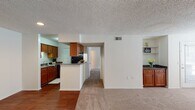This single-floor residence in Ashley Park, Richmond, VA offers a practical and well-organized layout throughout. The kitchen is equipped with warm wood cabinetry, granite-style countertops, black appliances including a refrigerator and dishwasher, and durable hardwood-style flooring. A peninsula with additional counter space connects the kitchen to the adjoining living and dining areas, which feature neutral carpet and a built-in cabinet nook with open shelving — a distinctive architectural detail adding both storage and character.

The living area is bright and open, benefiting from natural light through window treatments and access to an exterior door. Multiple bedrooms are carpeted and generously sized, each with windows that allow natural light and views of the surrounding neighborhood. One entry area features hardwood-style flooring, providing a practical transition space.

Two bathrooms serve the unit, each featuring granite-style countertops, single-basin sinks with wood vanity cabinetry, and shower/tub combinations. Textured ceilings are consistent throughout the home. The overall layout, visible in the 3D overview, reflects a compact yet functional design well-suited for comfortable everyday living.