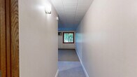 Located at 1111 S Seventh St in Minneapolis, MN, this single-floor unit offers an efficiently designed layout comprising a kitchen, bathroom, and hallway. The open living area features a combination of neutral carpet and large-format tile flooring, with a paneled ceiling overhead that runs throughout the space. A wood-framed window allows natural light to filter in, offering a view of surrounding greenery. A baseboard heating unit runs along the wall, providing reliable warmth during Minneapolis winters.

The kitchen is equipped with warm-toned oak cabinetry, both upper and lower, offering ample storage. It includes a white electric range, a full-size refrigerator, and a double-basin sink with dark countertops — all set atop easy-to-clean tile flooring. Recessed under-cabinet lighting adds functional illumination to the workspace.

The bathroom presents a clean, classic design with white hexagonal mosaic floor tile, a white vanity with a single-basin sink and paired cabinet doors below, a wall-mounted mirror, and a lighted vanity fixture above. The overall palette is crisp and bright, giving the bathroom a tidy, well-maintained appearance.

The hallway connects the rooms efficiently, contributing to the unit's practical and straightforward floor plan. The space is well-suited for those seeking a compact, functional living environment in Minneapolis.