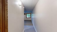 Located at 1111 S Seventh St in Minneapolis, MN, this single-floor unit offers an efficiently designed layout comprising a kitchen, bathroom, and hallway. The open living area features a combination of neutral carpet and large-format tile flooring, with a paneled ceiling overhead that runs throughout the space. A wood-framed window allows natural light to filter in, offering a view of surrounding greenery. A baseboard heating unit runs along the wall, providing reliable warmth during Minneapolis winters.

The kitchen is equipped with warm-toned oak cabinetry, both upper and lower, offering ample storage. It includes a white electric range, a full-size refrigerator, and a double-basin sink with dark countertops — all set atop easy-to-clean tile flooring. Recessed under-cabinet lighting adds functional illumination to the workspace.

The bathroom presents a clean, classic design with white hexagonal mosaic floor tile, a white vanity with a single-basin sink and paired cabinet doors below, a wall-mounted mirror, and a lighted vanity fixture above. The overall palette is crisp and bright, giving the bathroom a tidy, well-maintained appearance.

The hallway connects the rooms efficiently, contributing to the unit's practical and straightforward floor plan. The space is well-suited for those seeking a compact, functional living environment in Minneapolis.